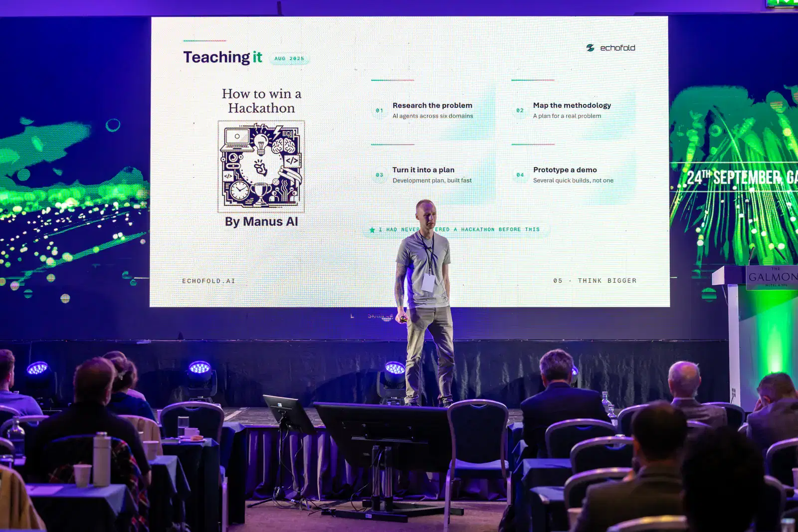 Kevin Collins on stage in front of a slide titled Teaching it, about the How to Win a Hackathon workshop with Manus AI