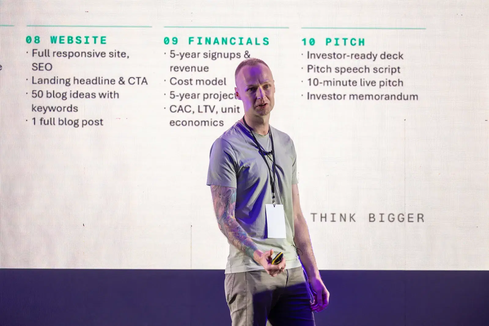 Kevin Collins mid-talk at the National AI Meet 2026, clicker in hand, beside a slide with the words Think Bigger